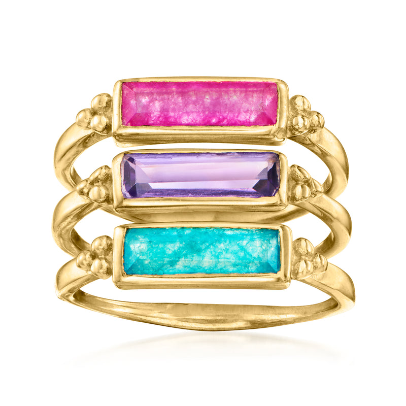 Three stacked gold-tone rings with rectangular pink, purple, and blue gemstones