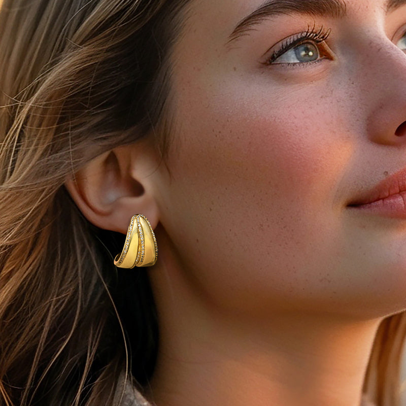 Small gold hoop earrings with white gemstone insets, worn close-up on ear