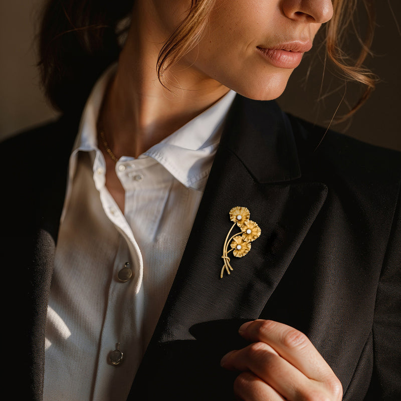 Gold flower pin with three white pearls on a dark blazer lapel
