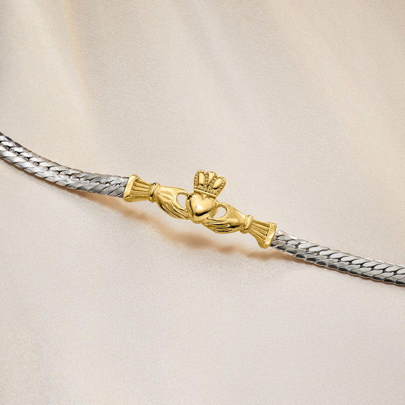 Close-up of sterling silver Cuban-link bracelet with gold claddagh heart and crown