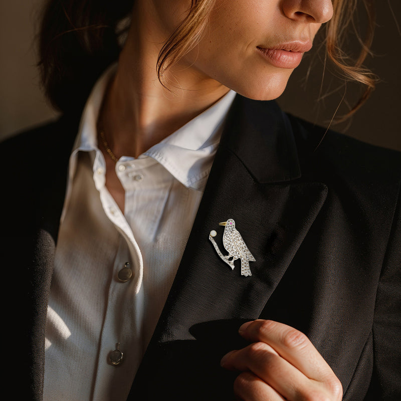 Bird pin on dark blazer lapel with cultured pearl body, ruby eye, and diamond accents