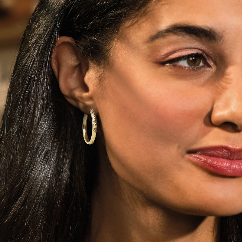 Gold diamond-cut flat hoop earrings on ear