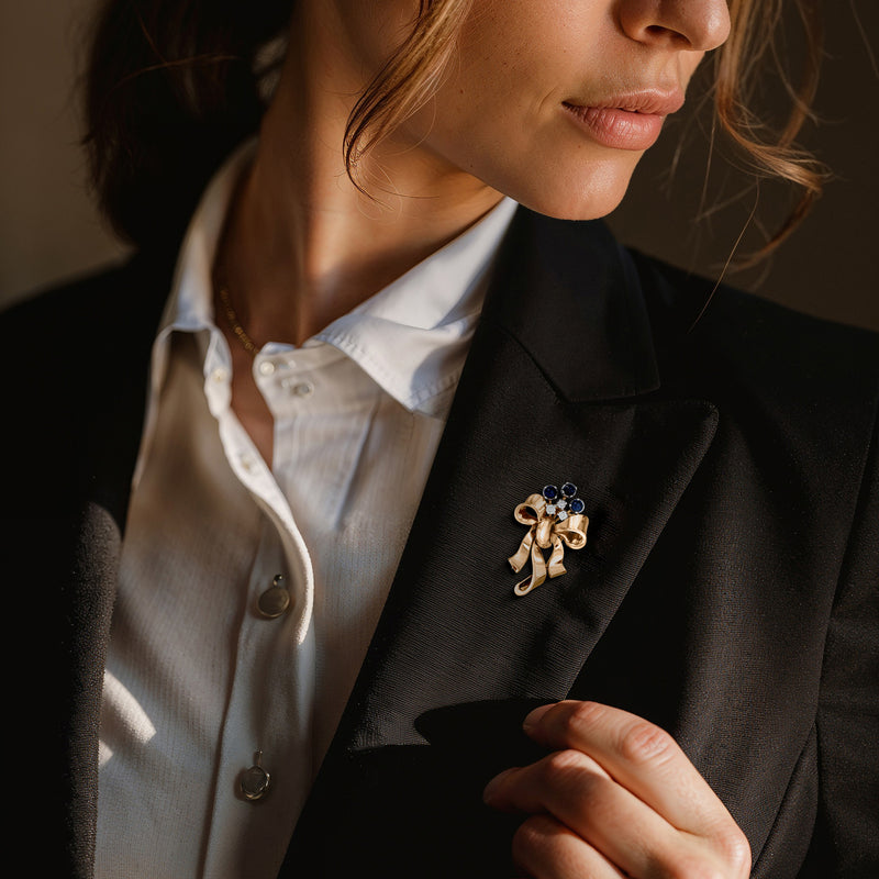 Gold bow pin on blazer lapel with blue sapphire and white diamond accents