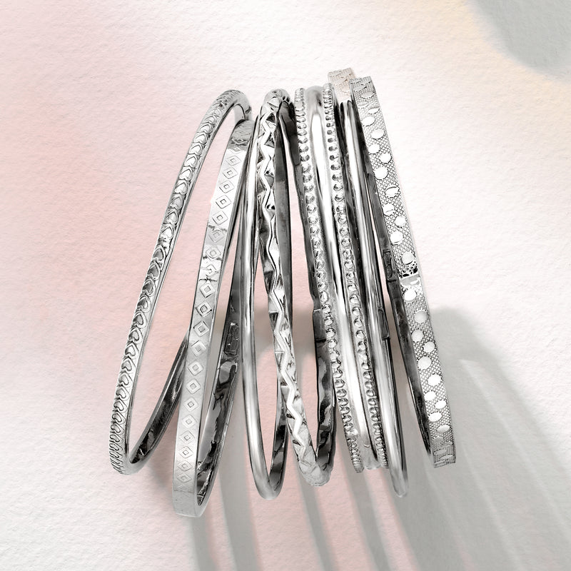 Stack of seven sterling silver bangles with different textured finishes and edges