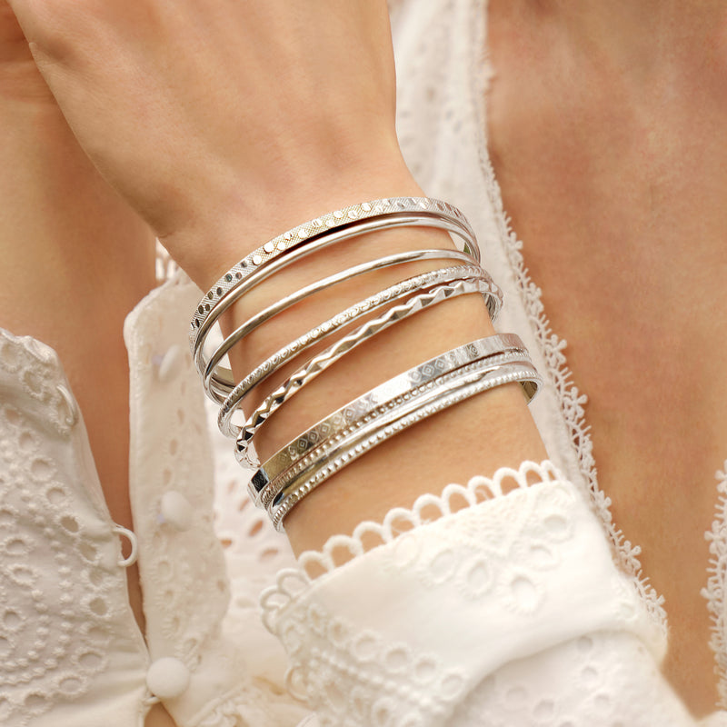 Sterling silver bangles on wrist, assorted textured bands with thin polished layers