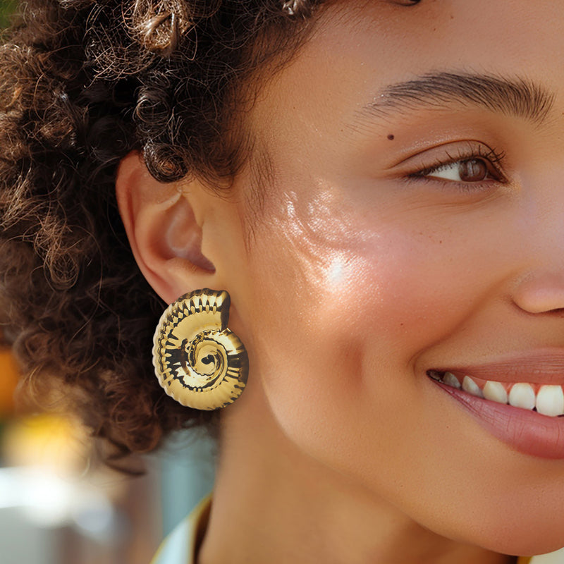 Gold seashell spiral stud earrings worn on ear, ridged swirl design