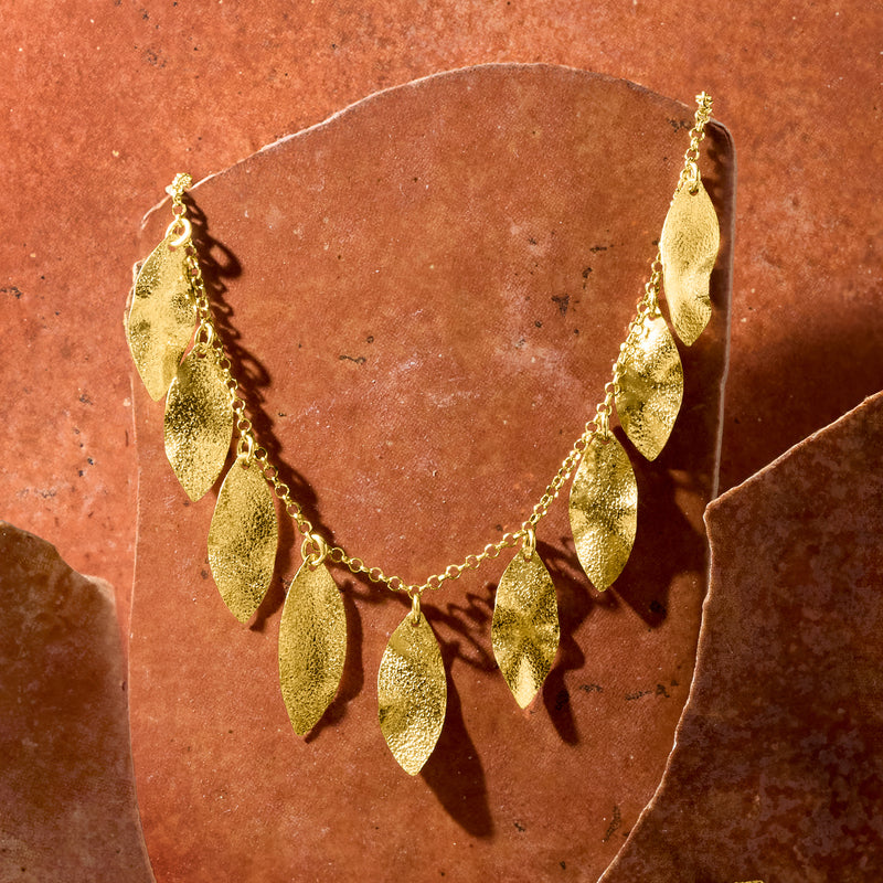 Close-up gold leaf station necklace with textured teardrop leaf charms on chain