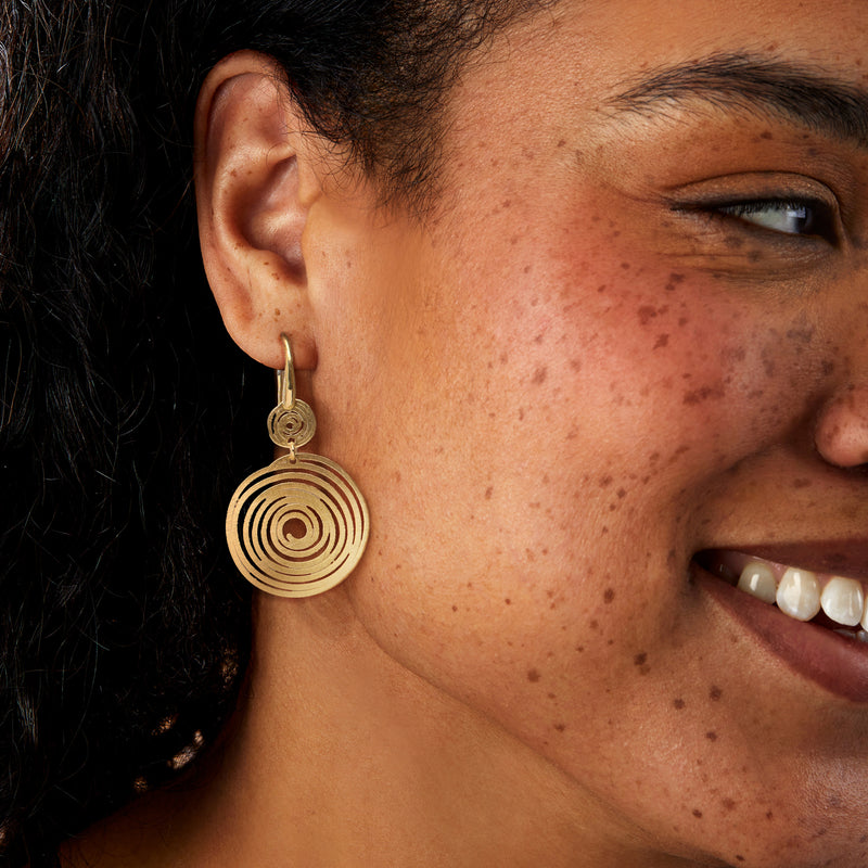 Gold spiral disc drop earrings on ear, concentric swirl round dangle