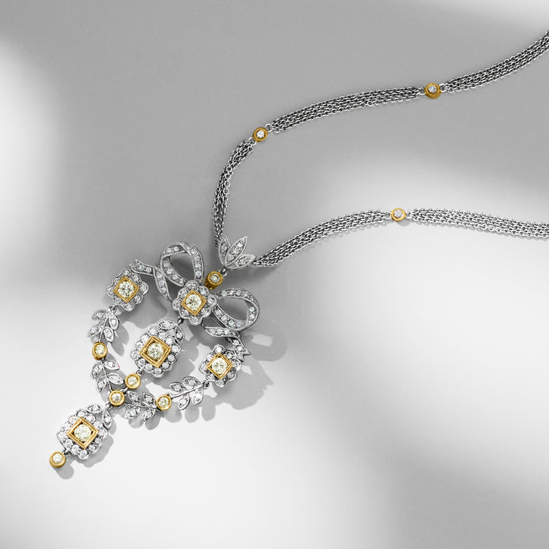 Two-tone gold diamond pendant on chain, close view of heart-bow design with yellow accents