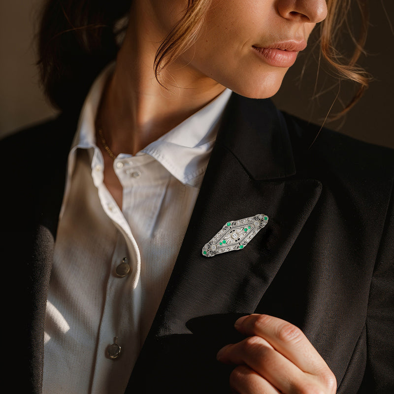 Oval filigree gemstone pin on dark blazer lapel with green and clear stones