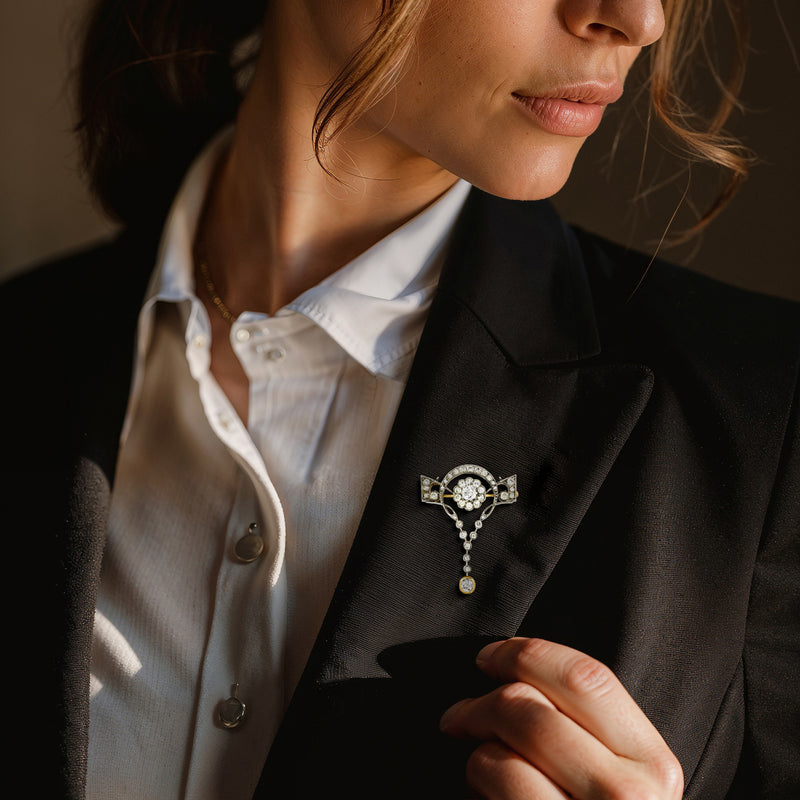 Diamond floral pin on black blazer lapel with dangling round gold-and-silver drops