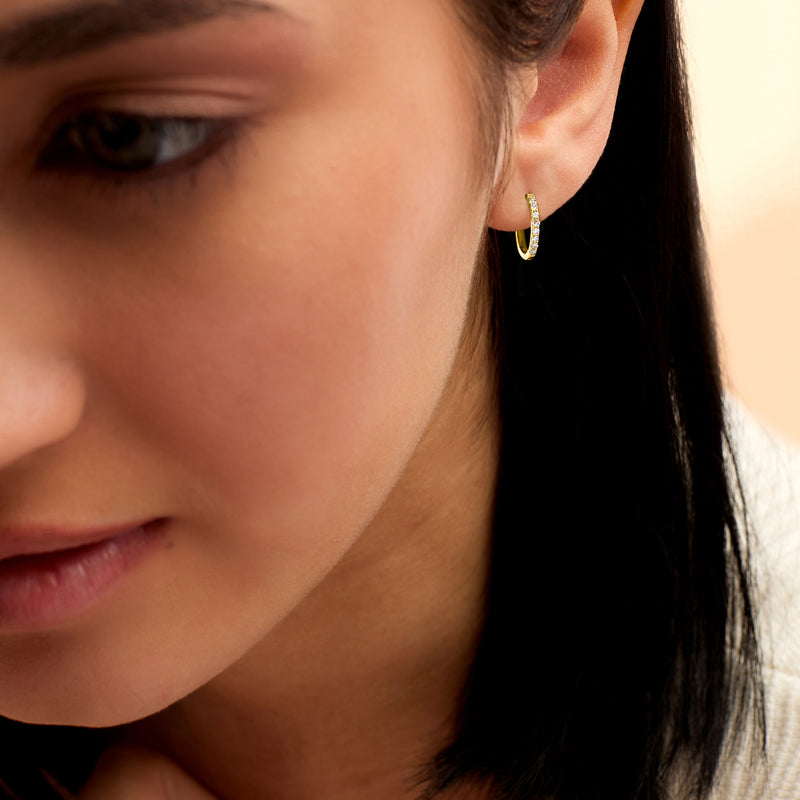 Woman wearing 14kt yellow gold diamond huggie hoop earrings on ear