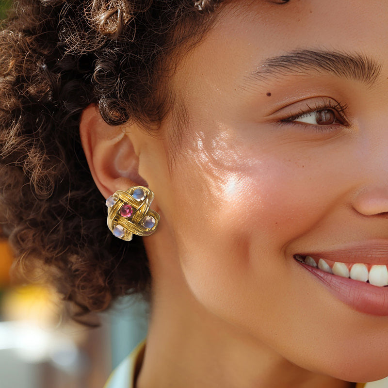 Woven gold stud earrings with blue moonstone and pink accents, worn on ear