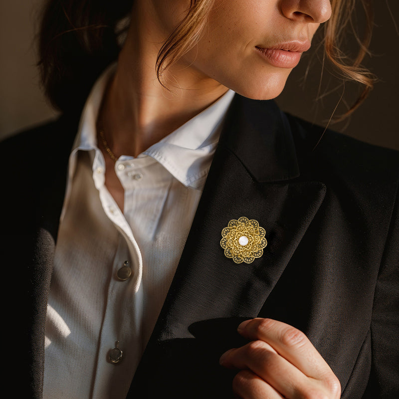 Gold filigree flower pin with round white pearl on suit lapel