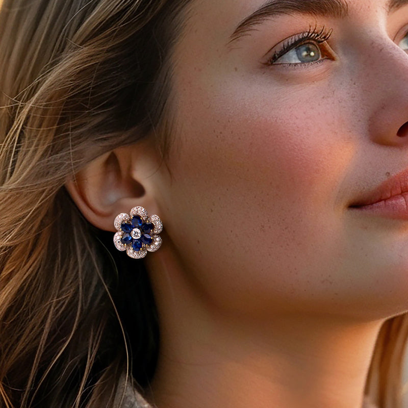 Blue sapphire and diamond flower stud earrings on ear in two-tone gold