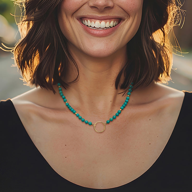 Turquoise bead necklace with open-circle gold pendant on neckline close-up