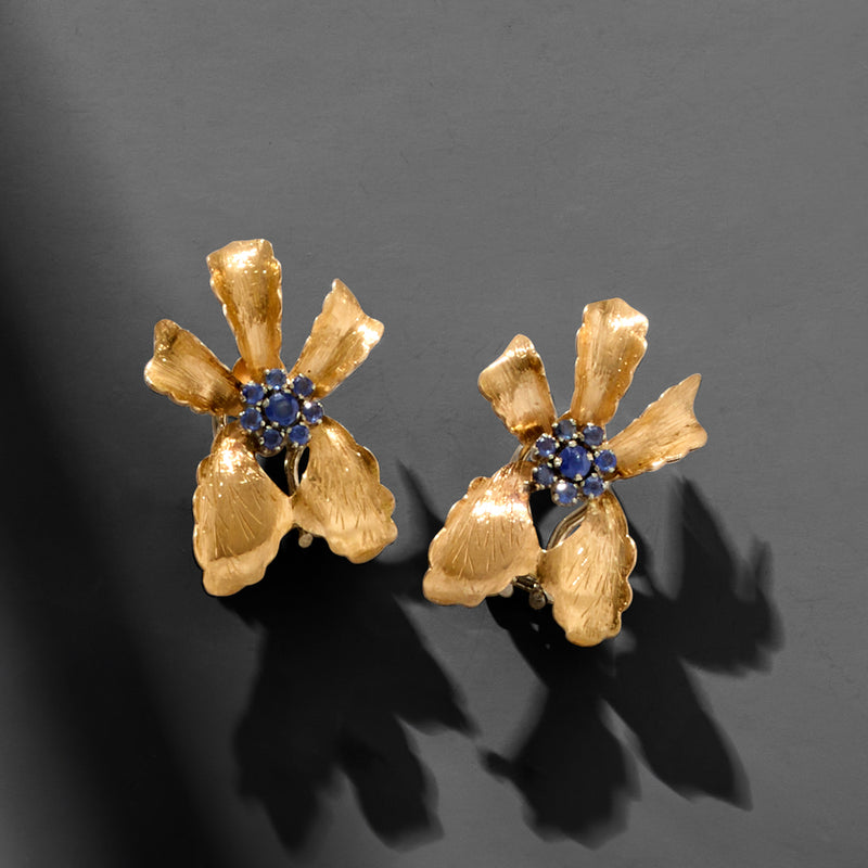 Gold flower stud earrings with blue sapphire center and raised petal texture
