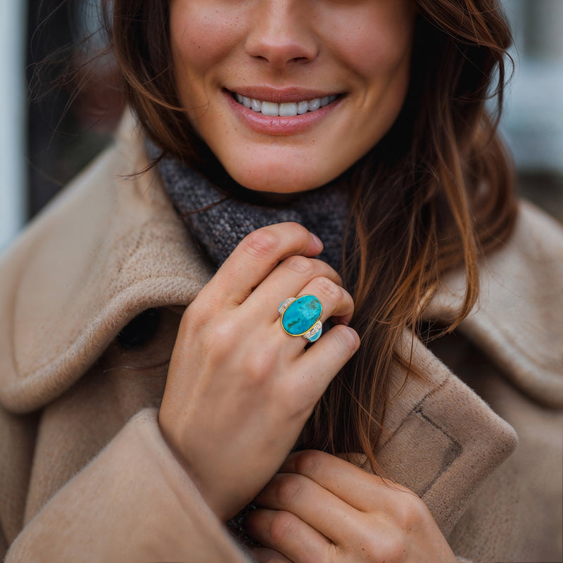 Turquoise oval gemstone ring with diamond band, worn on a hand