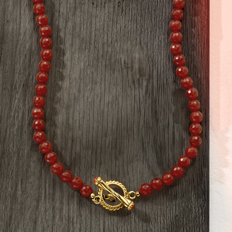 Red carnelian bead necklace with gold toggle clasp, close-up on dark display
