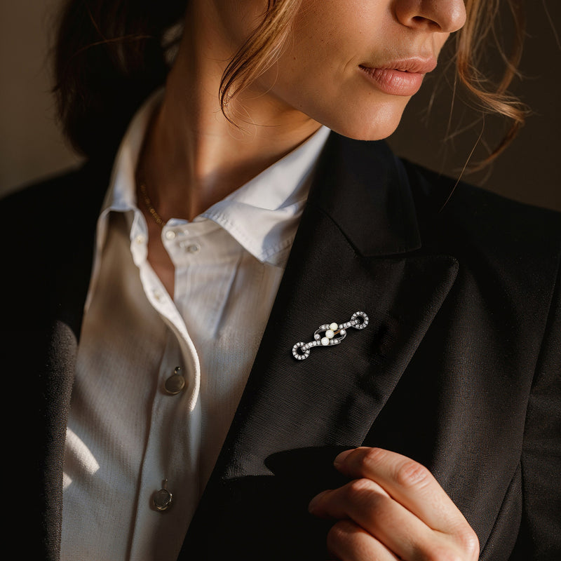 Pearl and diamond lapel pin on dark blazer, three round white pearls and silver setting