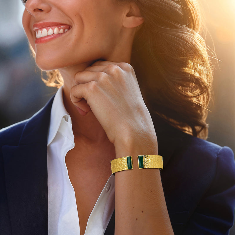 Gold cuff bracelet with two green square stones on wrist