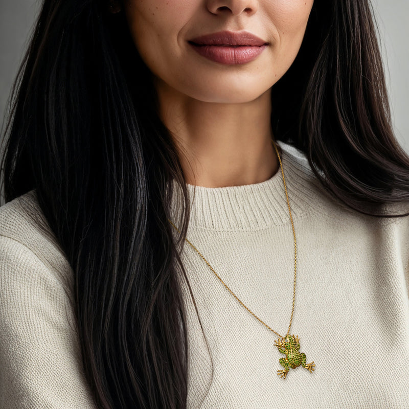 Gold frog pendant necklace with green gem frog and black eyes, worn on a chain