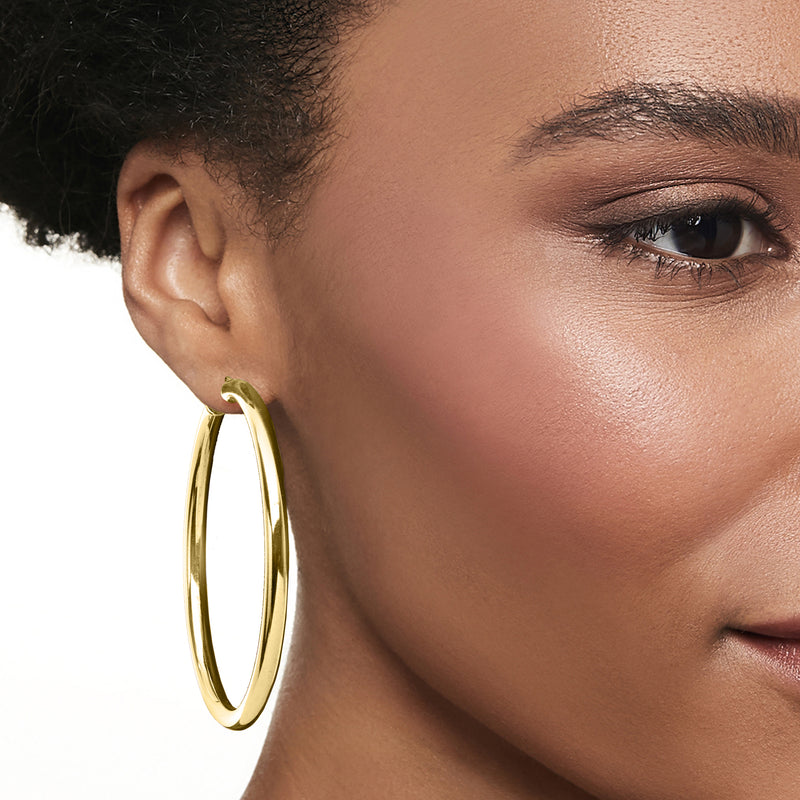 Gold-tone hoop earring on model ear, smooth polished oval loop