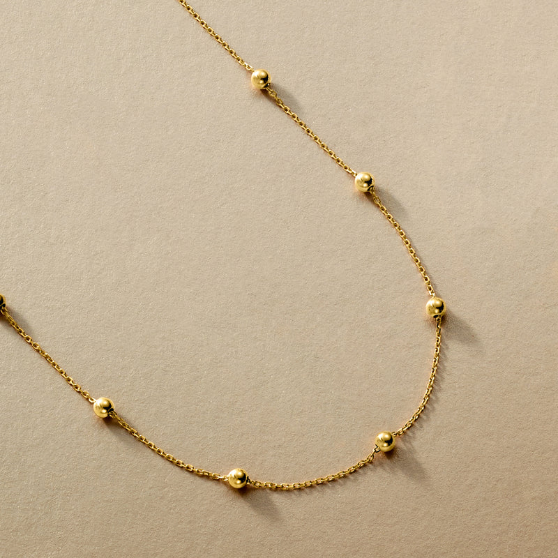 Close-up of 10kt yellow gold bead station necklace with round beads on a chain
