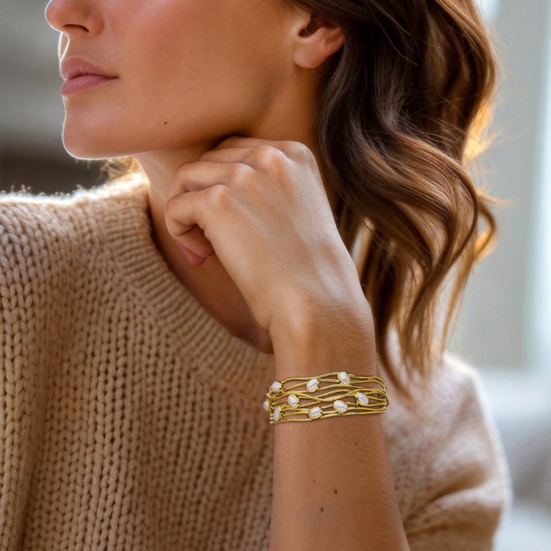 Gold cuff bracelet with small cultured pearls worn on wrist