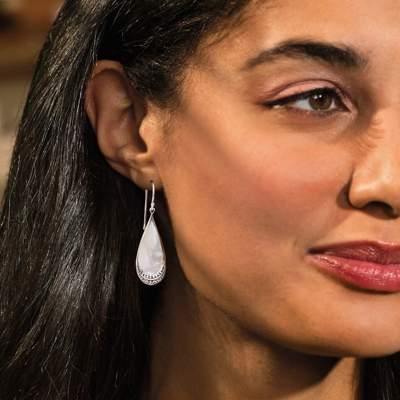 Sterling silver teardrop mother-of-pearl earrings with engraved border, worn on ear