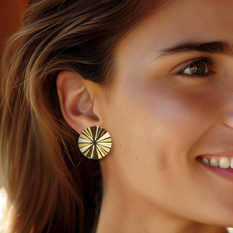 Gold-tone round sunburst stud earrings on model’s ear, faceted ridged texture