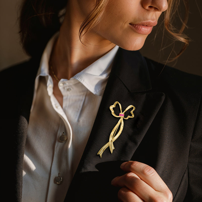 Yellow gold ribbon pin with ruby accents on a blazer lapel