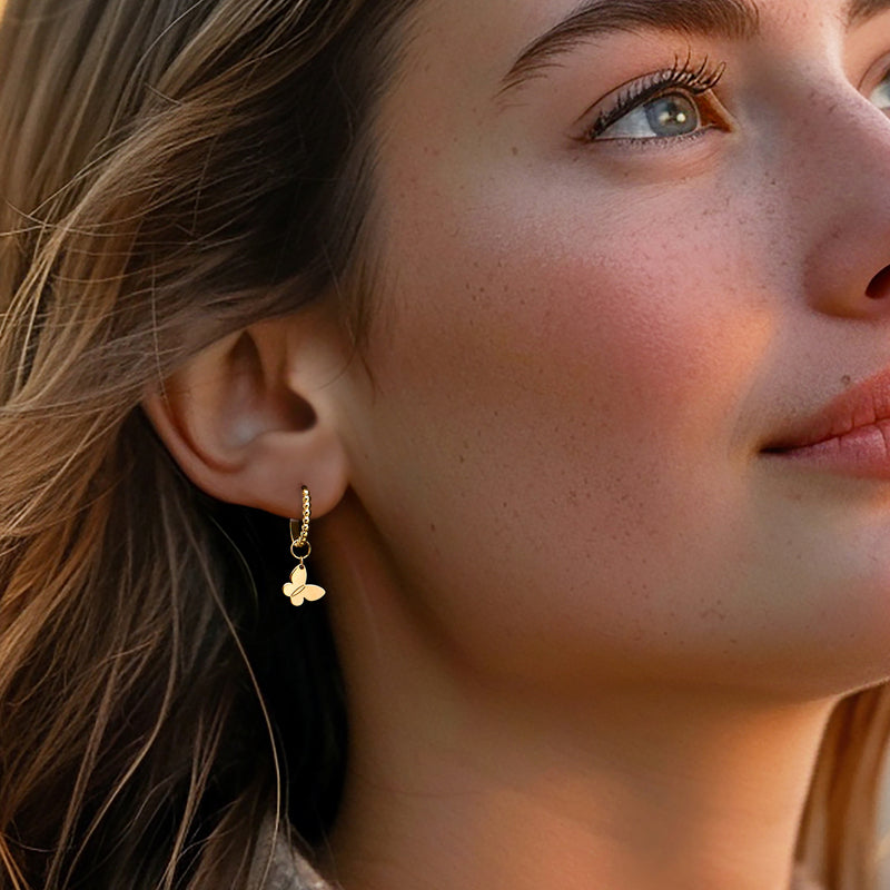 Butterfly charm hoop earrings in yellow gold worn on model’s ear