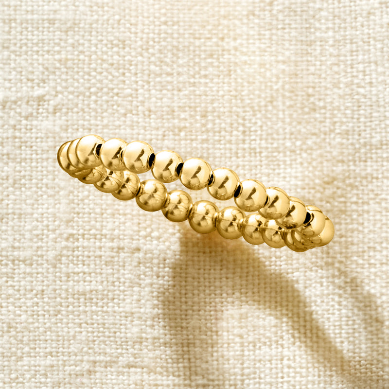Yellow gold bead stretch ring close-up, shiny round beads on fabric