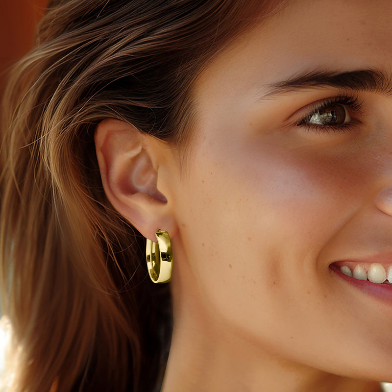 Oval 14kt yellow gold hoop earrings on ear, polished reflective oval hoops