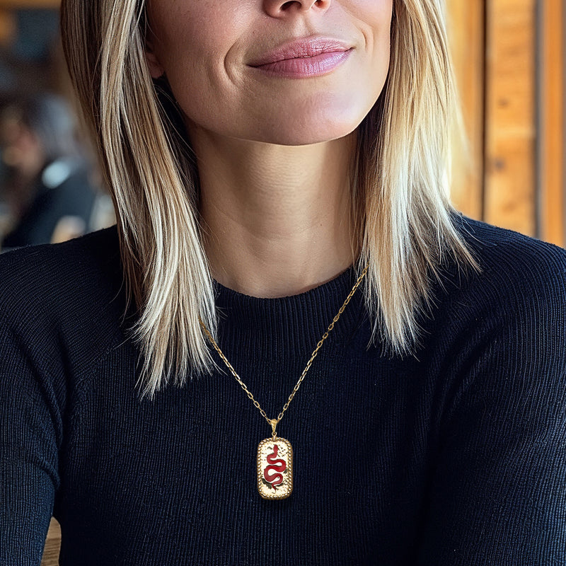Gold chain snake pendant necklace with red enamel snake charm on textured oval bezel