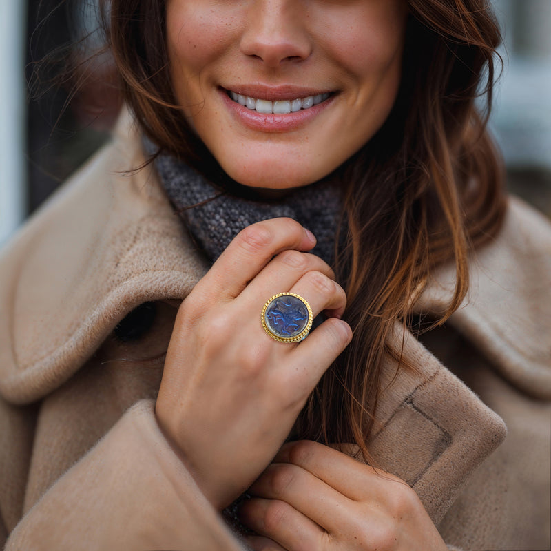 Gold lion cameo ring on hand, oval blue face with beaded rim and teal stone