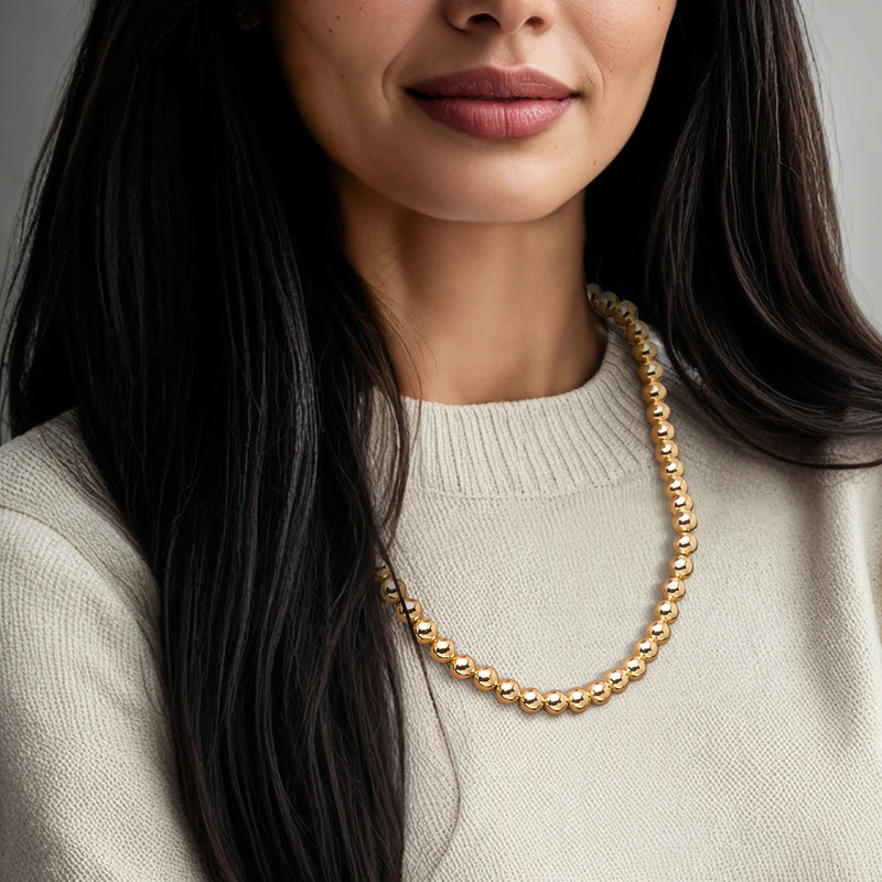 Gold bead necklace worn over a cream sweater neckline.