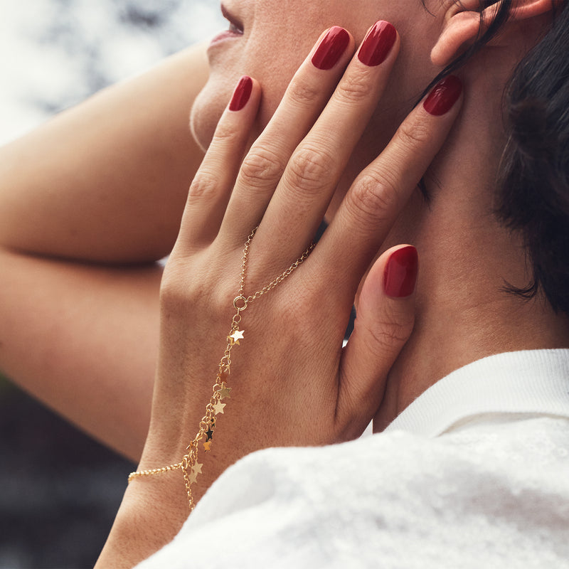 Gold-tone star hand chain bracelet worn on hand, with small dangling star charms