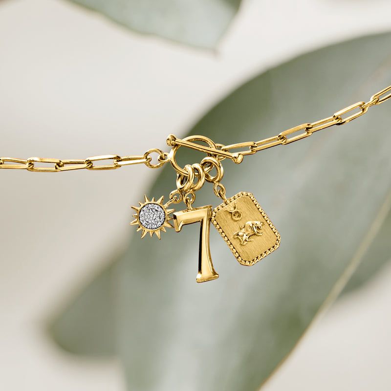 Gold charm necklace with round sun diamond charm, letter T charm, and small pendant