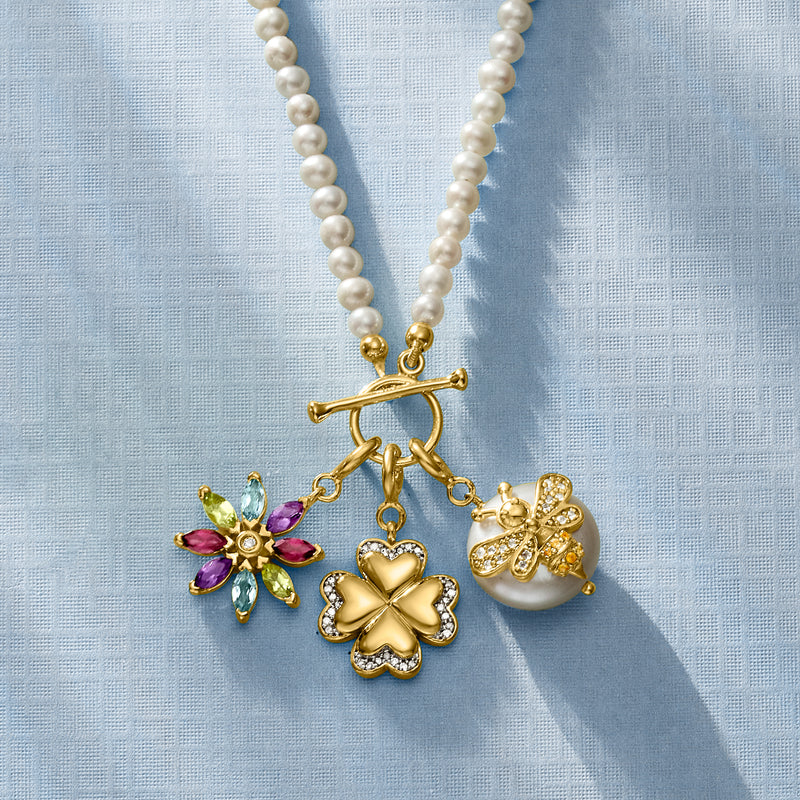 Gold four-leaf clover charm beside heart charm and purple flower charm