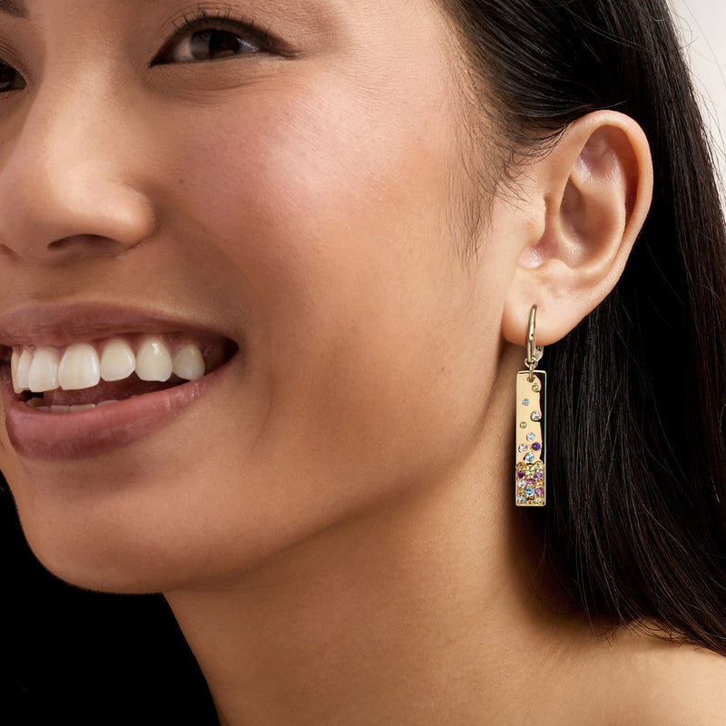 Gold leverback drop earrings with colorful gemstones, worn by model