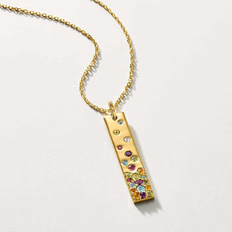 Gold bar pendant necklace with scattered multicolor gemstones and dangling chain