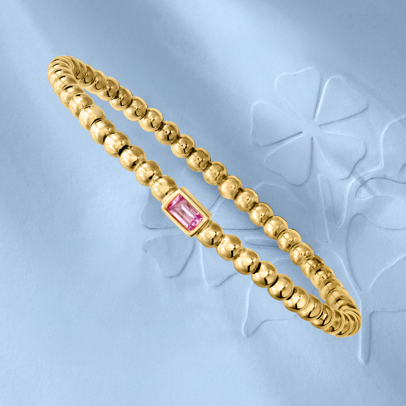 Gold beaded stretch bracelet with pink square sapphire accent, angled view.
