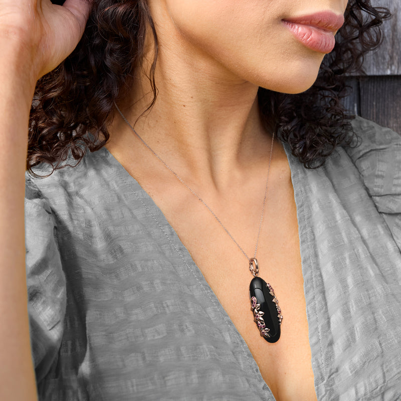 Rose gold chain necklace with black oval pendant and pink gem cluster, worn on neck