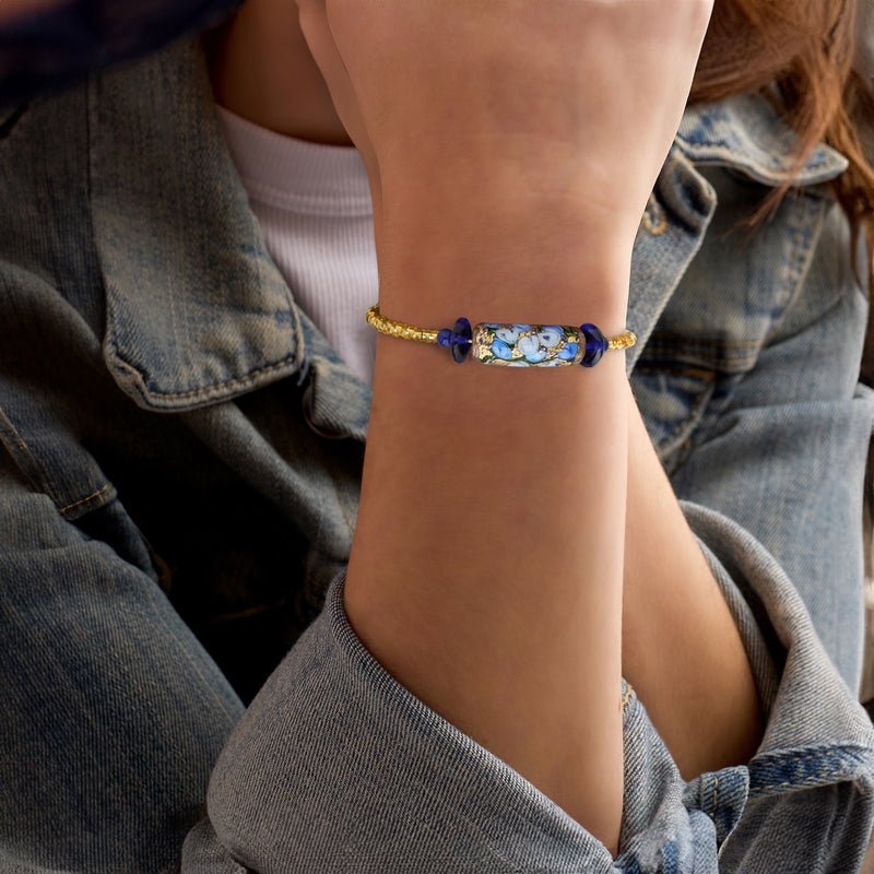 Blue floral glass center beaded wrap bracelet on wrist, with gold beads and navy charms