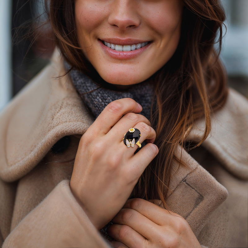 Gold-tone ring with black oval stone and white crystal butterfly bow, worn on hand