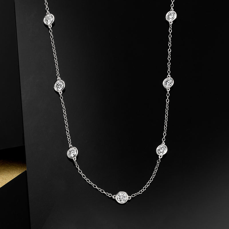 White gold station necklace featuring round bezel-set diamonds along a slender chain