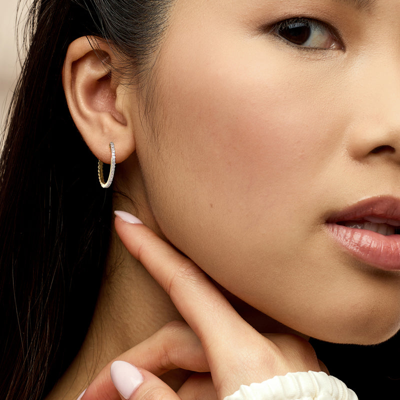 Gold-tone beaded hoop earrings with small white stones, worn on model