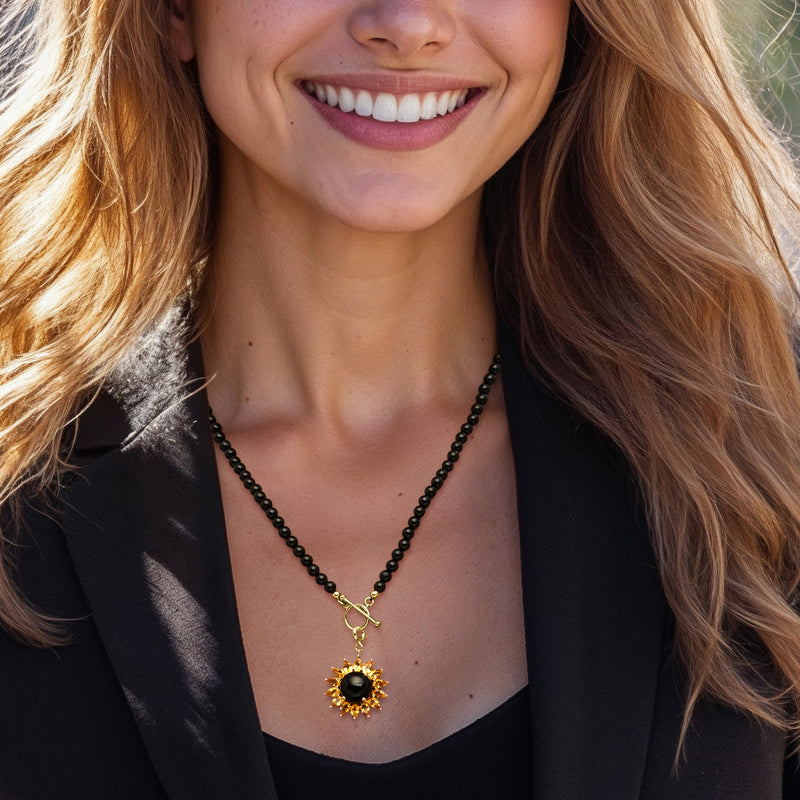 Gold-tone flower charm on black beaded necklace, worn at neckline with black center